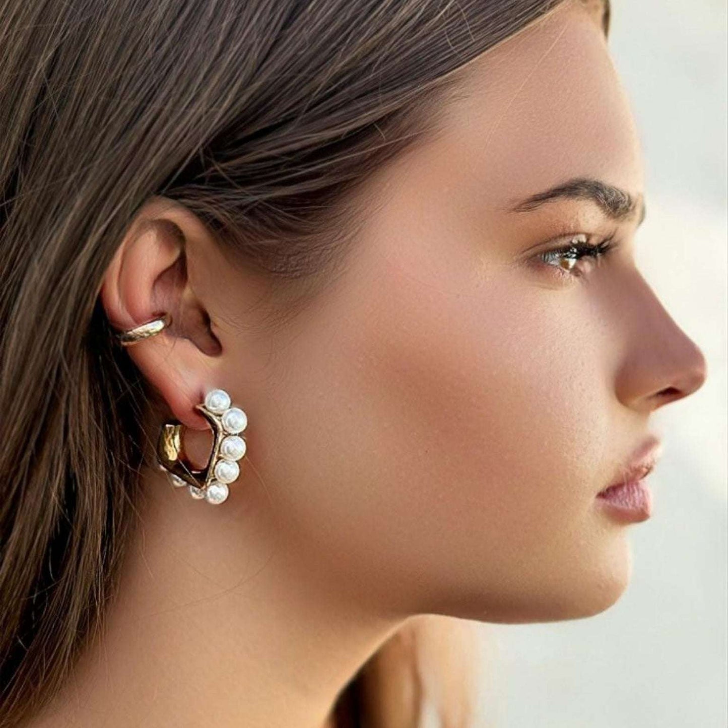 Brincos Zoe em aço inoxidável dourado com pérolas simuladas, mostrando o design sofisticado e contemporâneo.