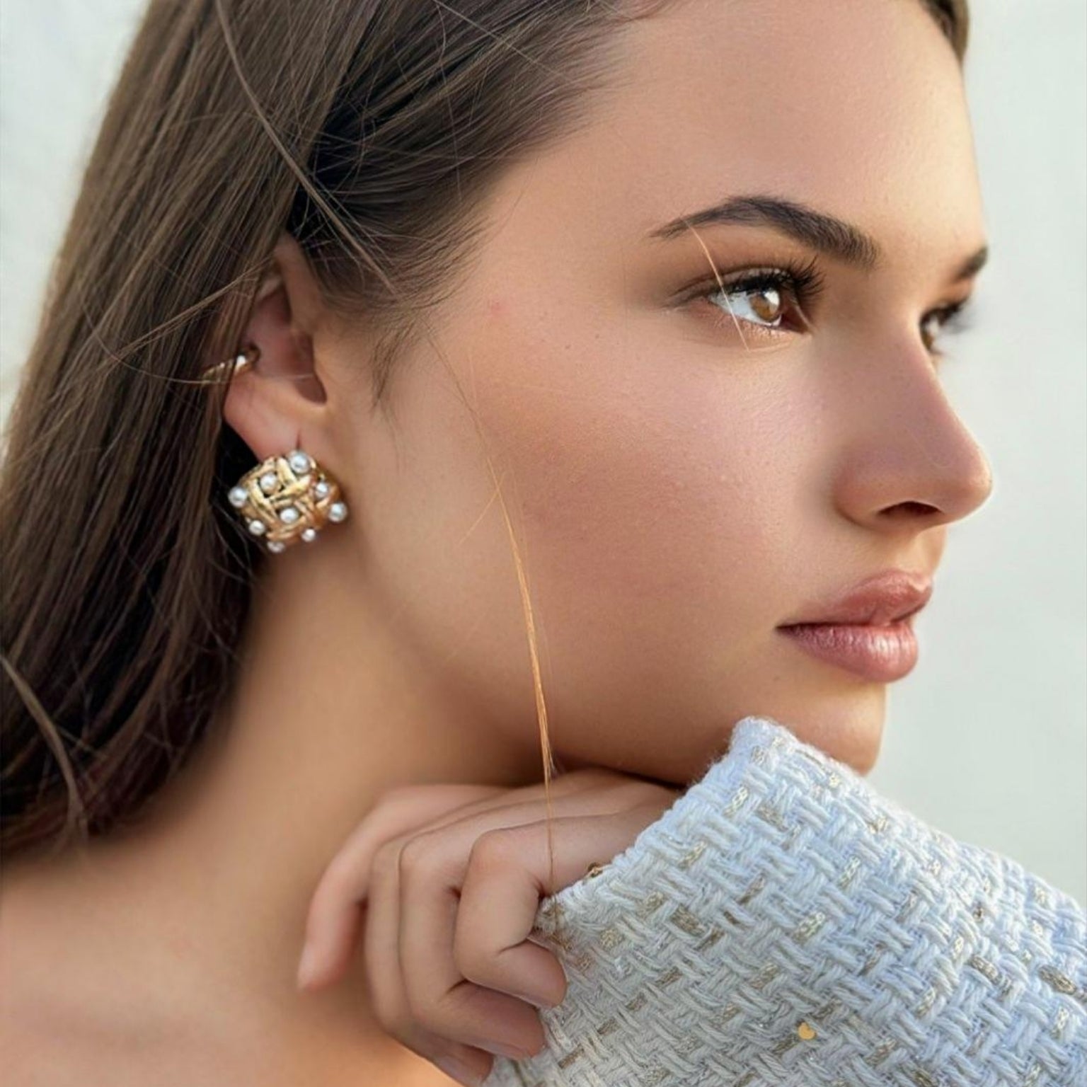 Modelo a usar os brincos Ivy em aço inoxidável dourado com design entrelaçado e pérolas simuladas, mostrando a elegância e o ajuste perfeito ao visual casual.